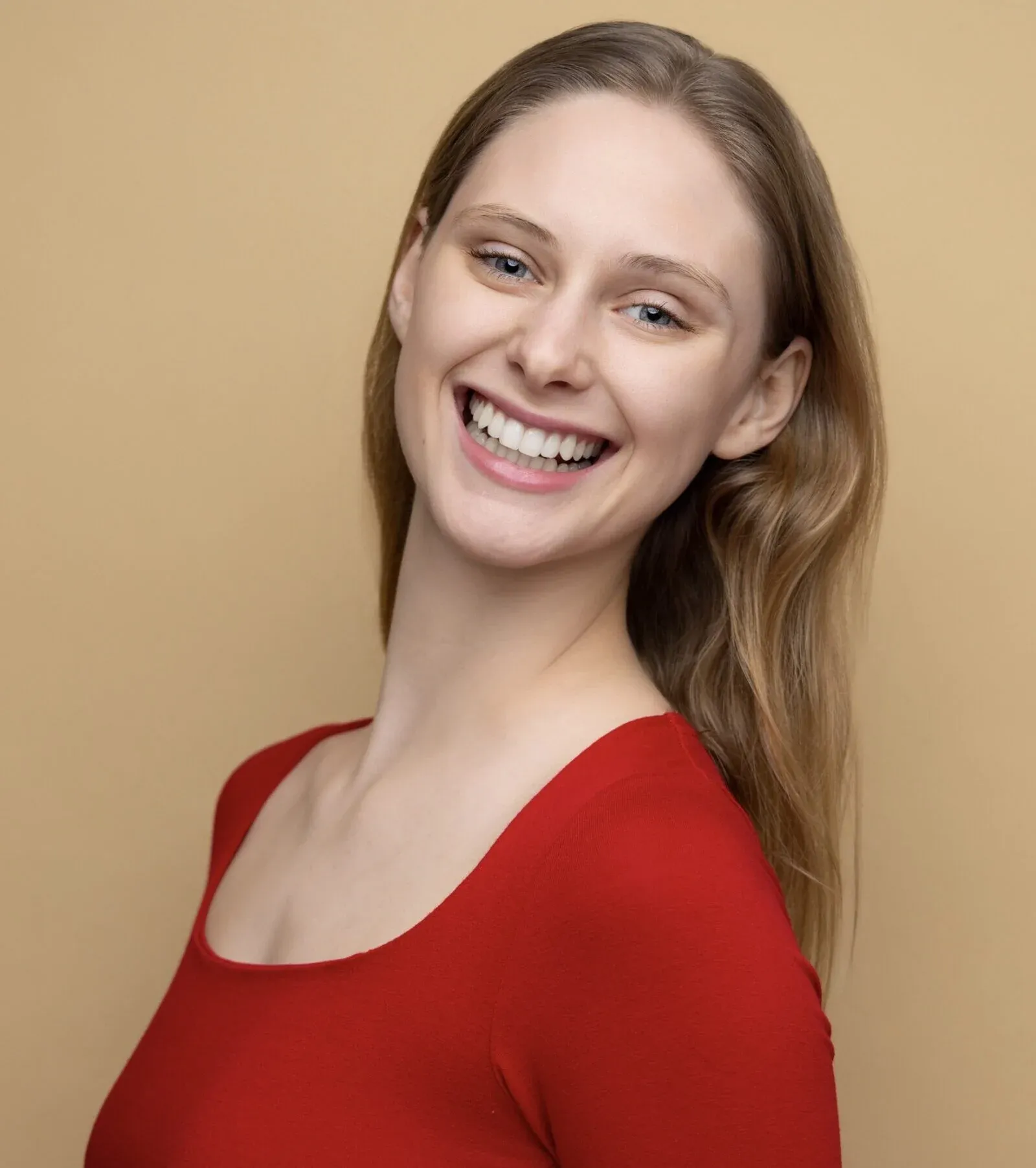 Cordelia June Reynolds, smiling broadly in a red top against a warm tan backdrop